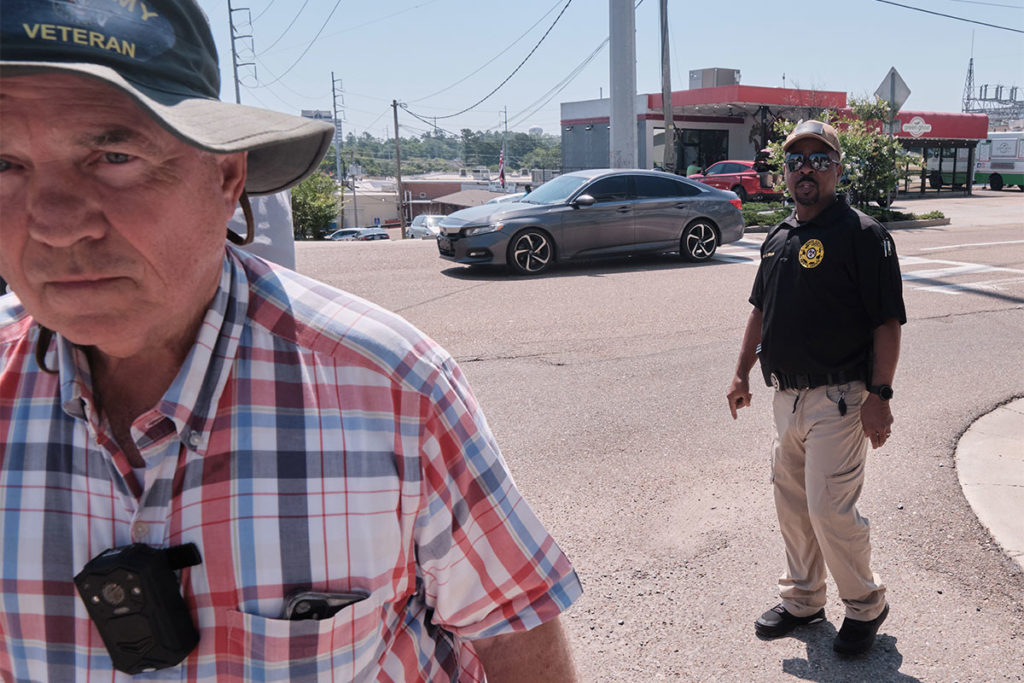 A sheriff stands in the road looking at the retreating back of a white man