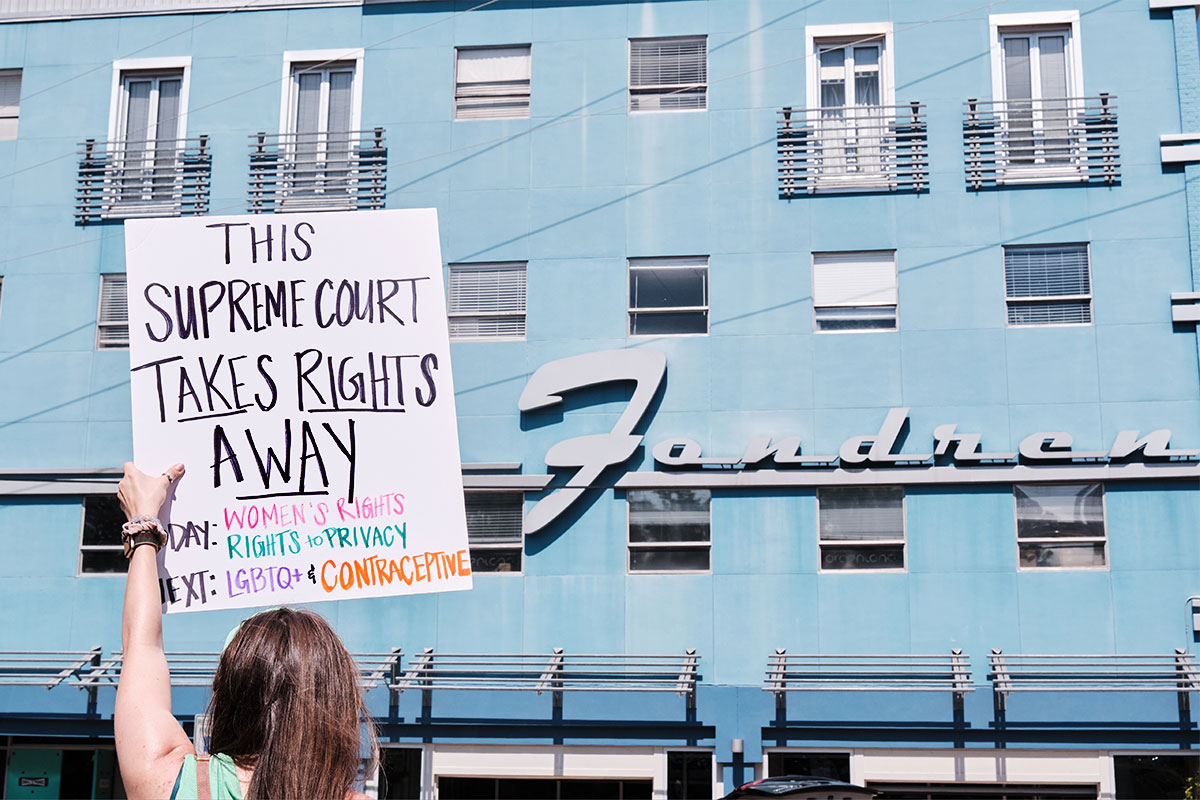 "This Supreme Court Takes Rights Away" sign held aloft in front of the blue Fondren building