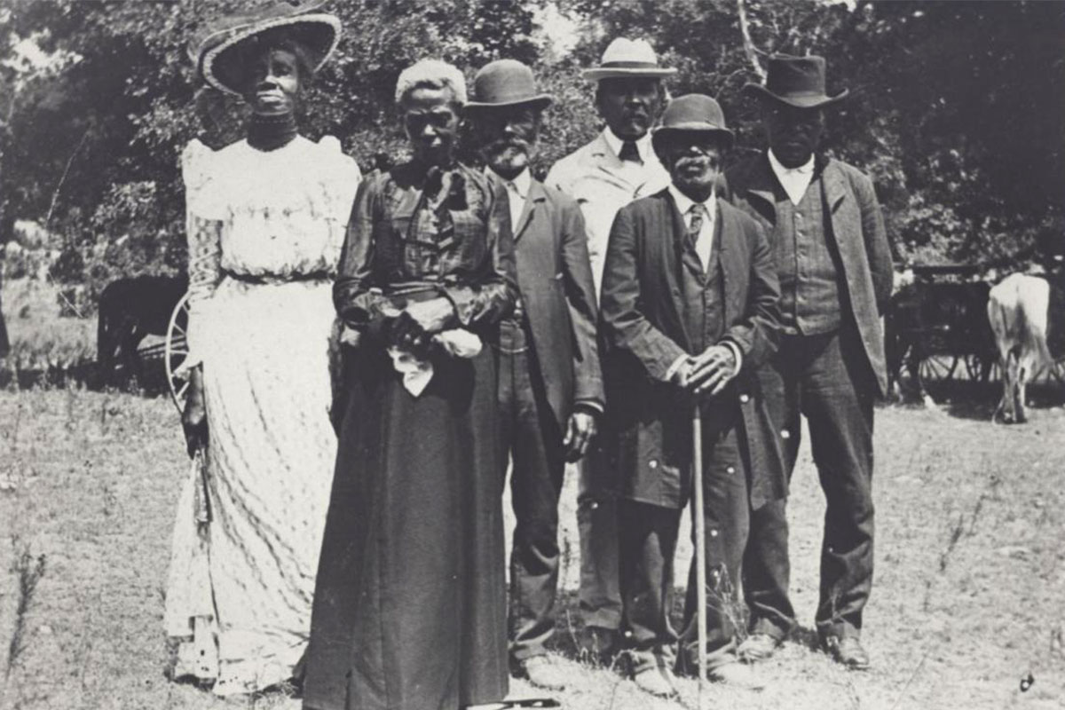 Six black people in formal wear pose for an old black and white photo