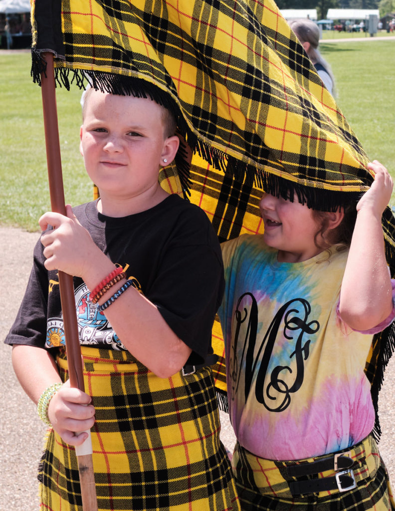 Two kids in yellow tartan hold a large matching flag