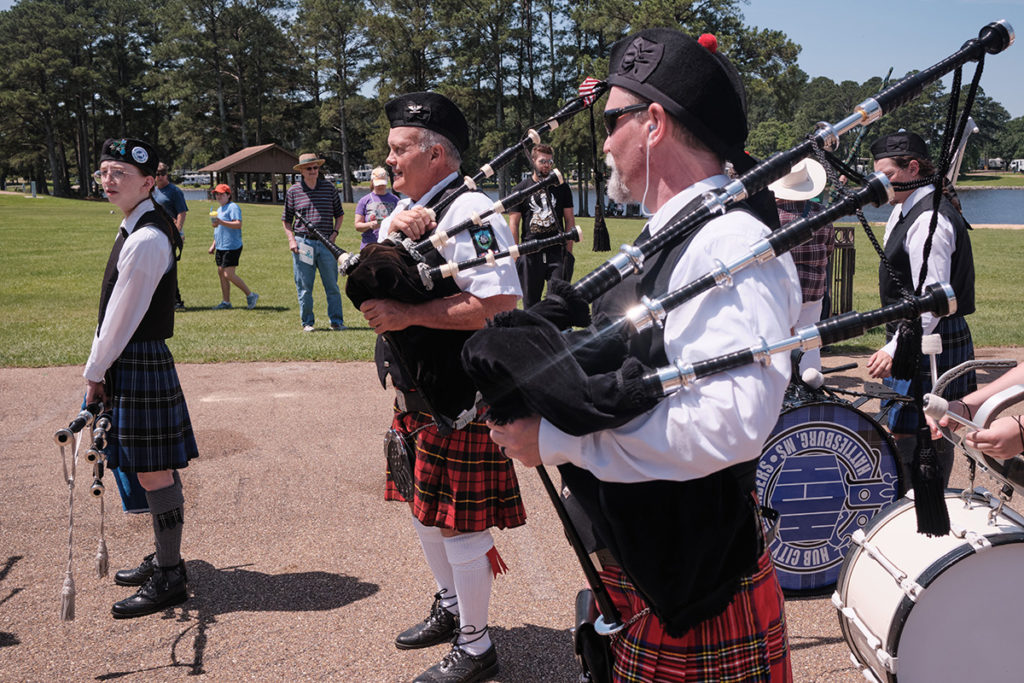People in tartan stand in line holding bagpipes and drums
