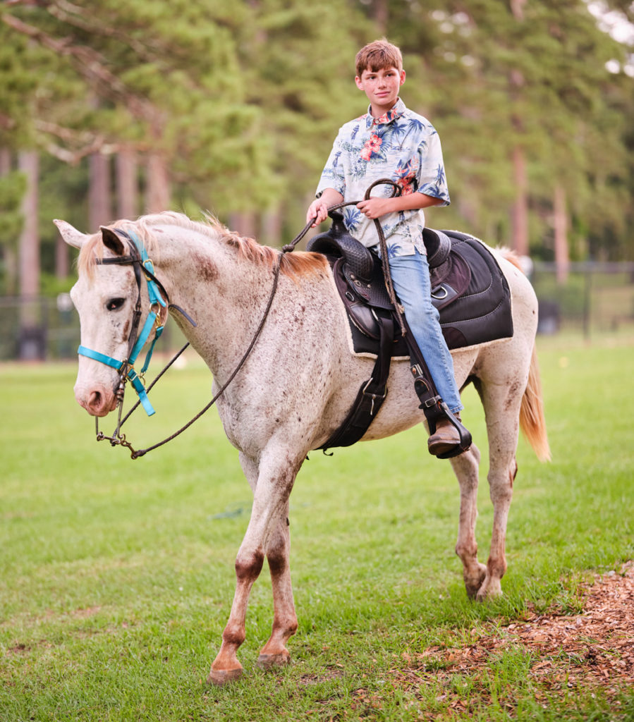 A youth sits astride a cream colored horse