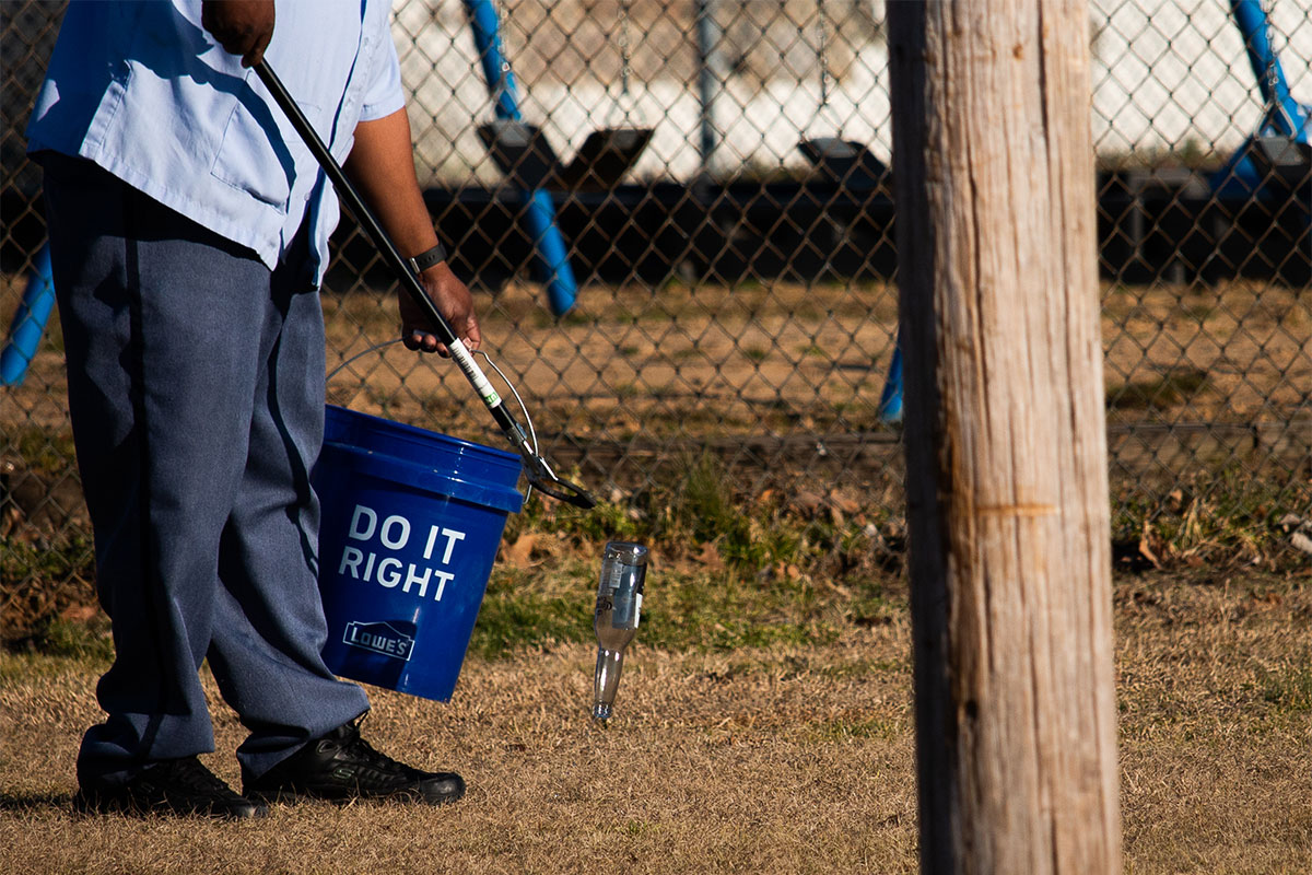 a close up of a man picking up a glass bottle to put inside a blue bucket
