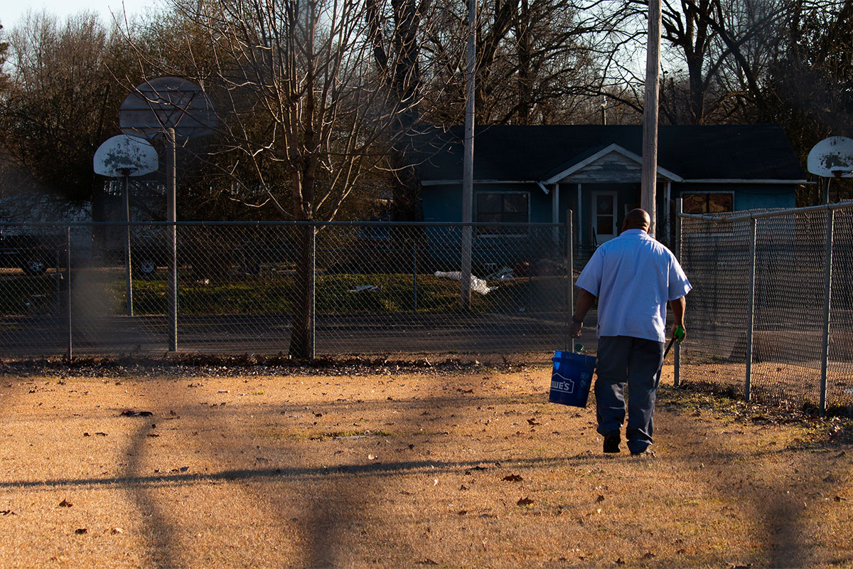 A man walks through a sport field picking up litter into a blue bucket