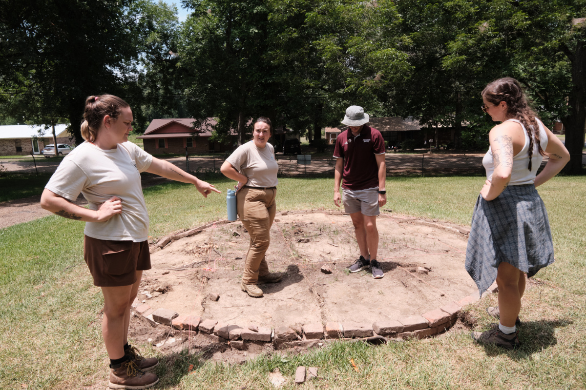 Four people standing around a circle of cleared earth with brick border