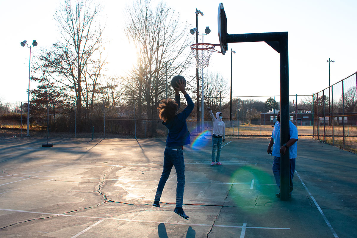 Three people play basketball as the sun begins to set
