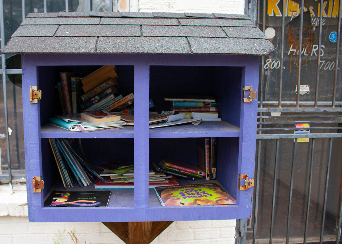 Outside of a store stands a purple box on a stand with little roofing, the interior shelves containing books