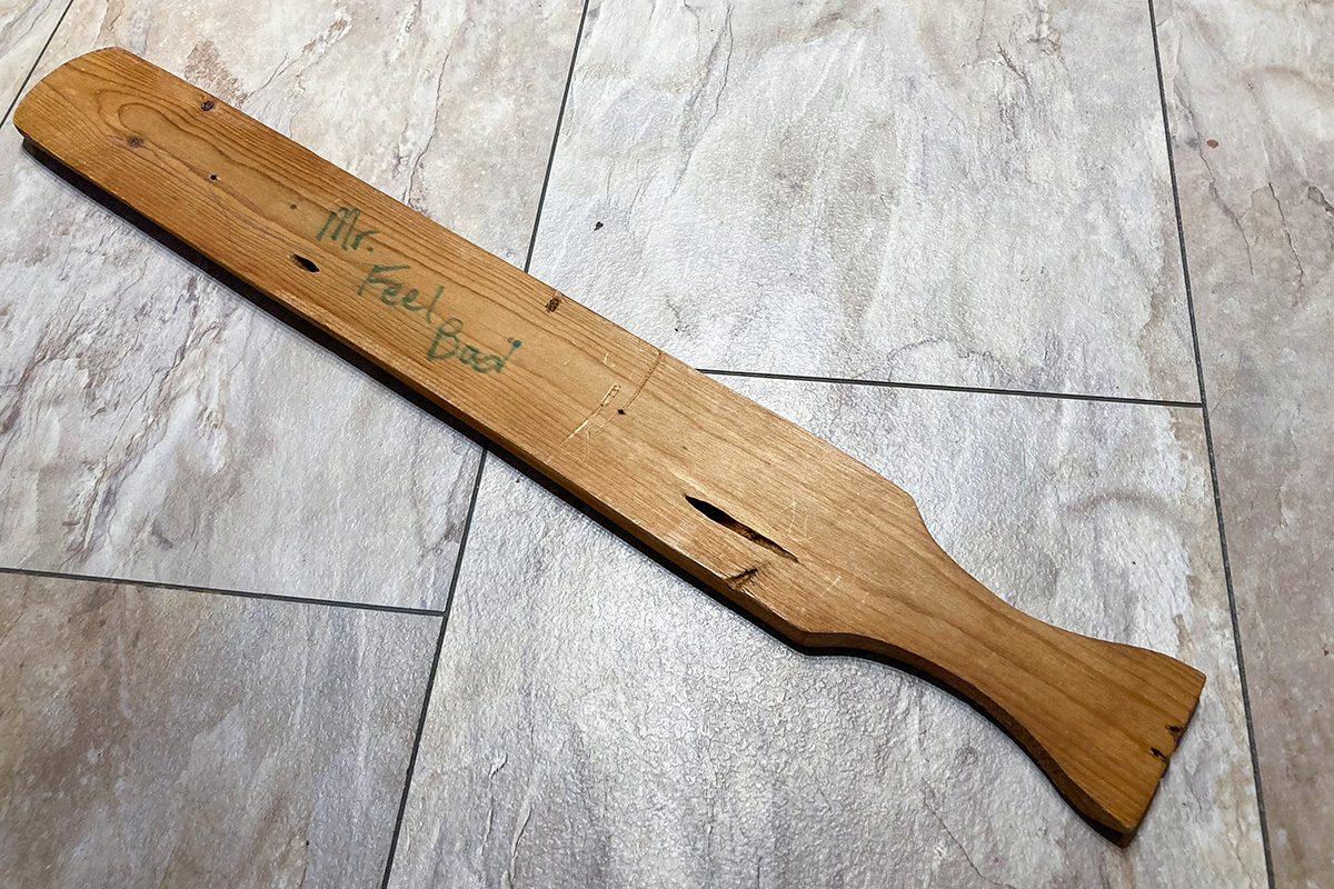 A wooden paddle that has "Mr. Feel Bad" written on it in green marker