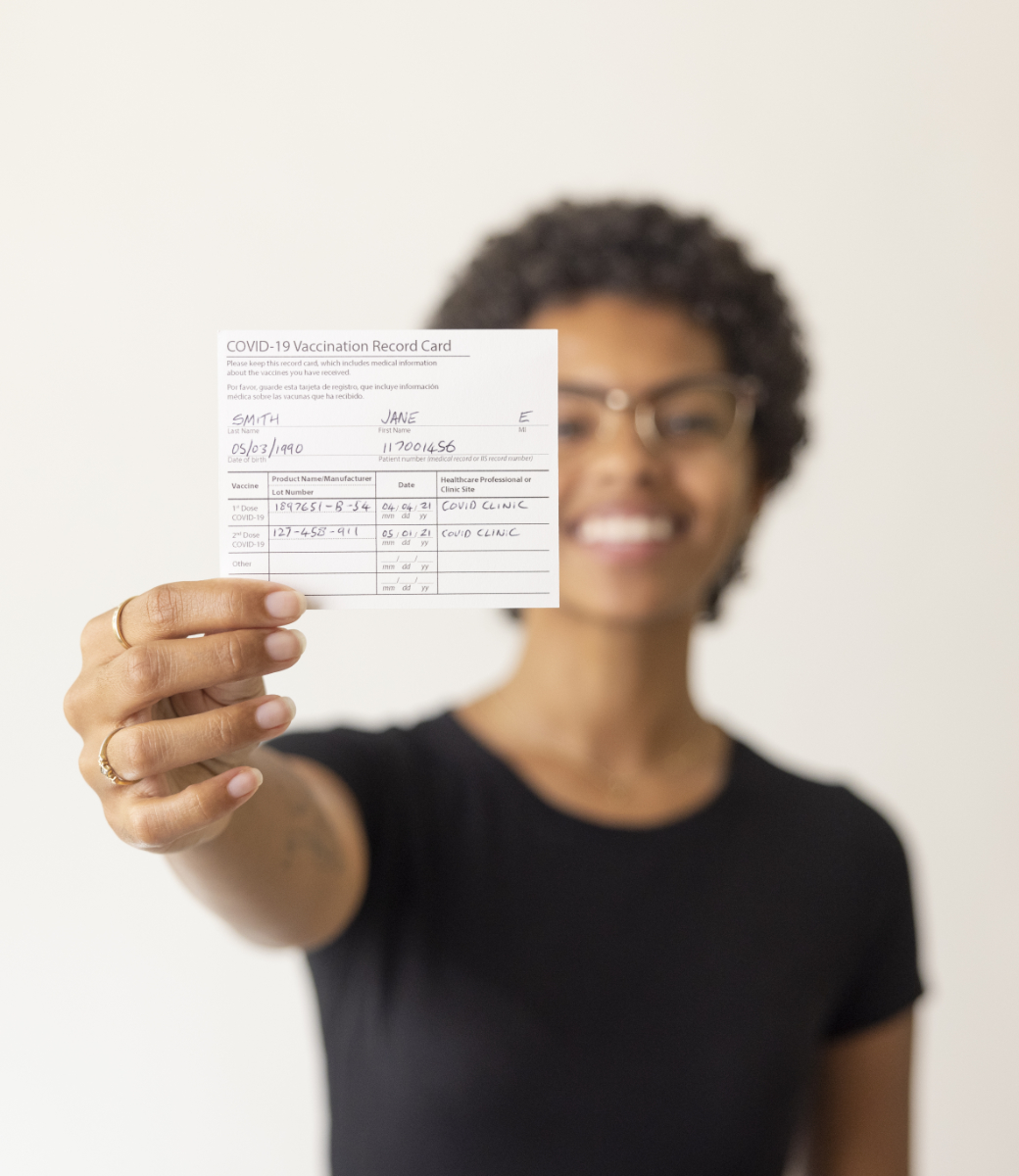 out of focus smiling woman extends her arm holding vaccination record card