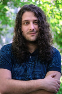 Long haired man posed with arms crossed and slight smile.
