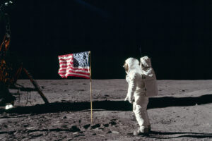 An astronaut standing on the surface of the moon, a US flag beside him