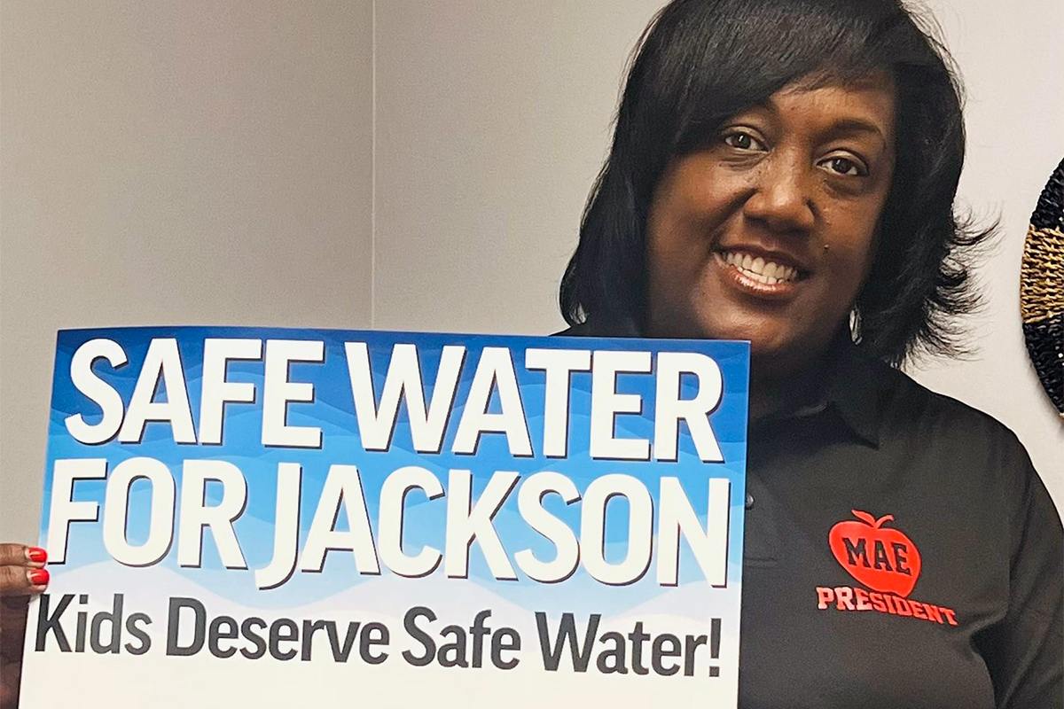 A woman holding a sign that says Safe Water for Jackson, Kids Deserve Safe Water!