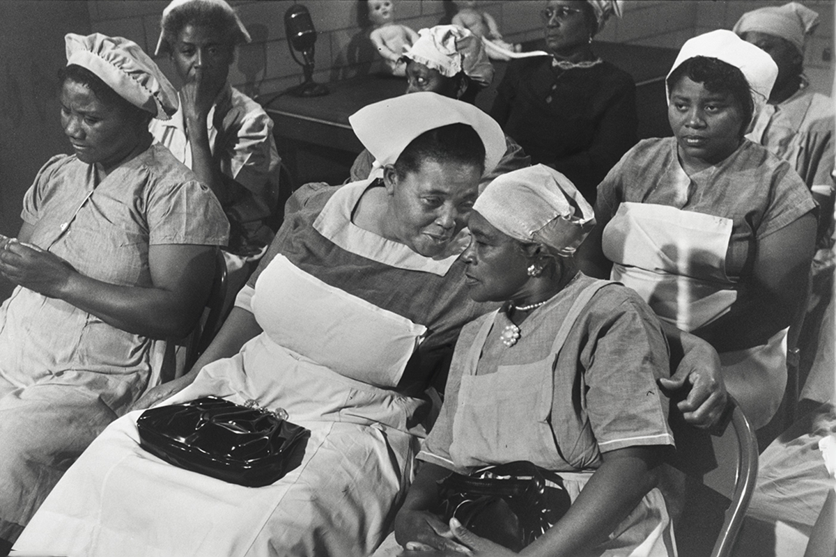 A black and white photo of Black midwives in nurse uniforms sitting together in a room