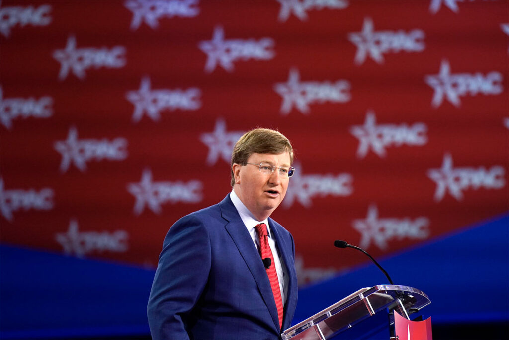 A man in a blue suit in front of a red white and blue CPAC background