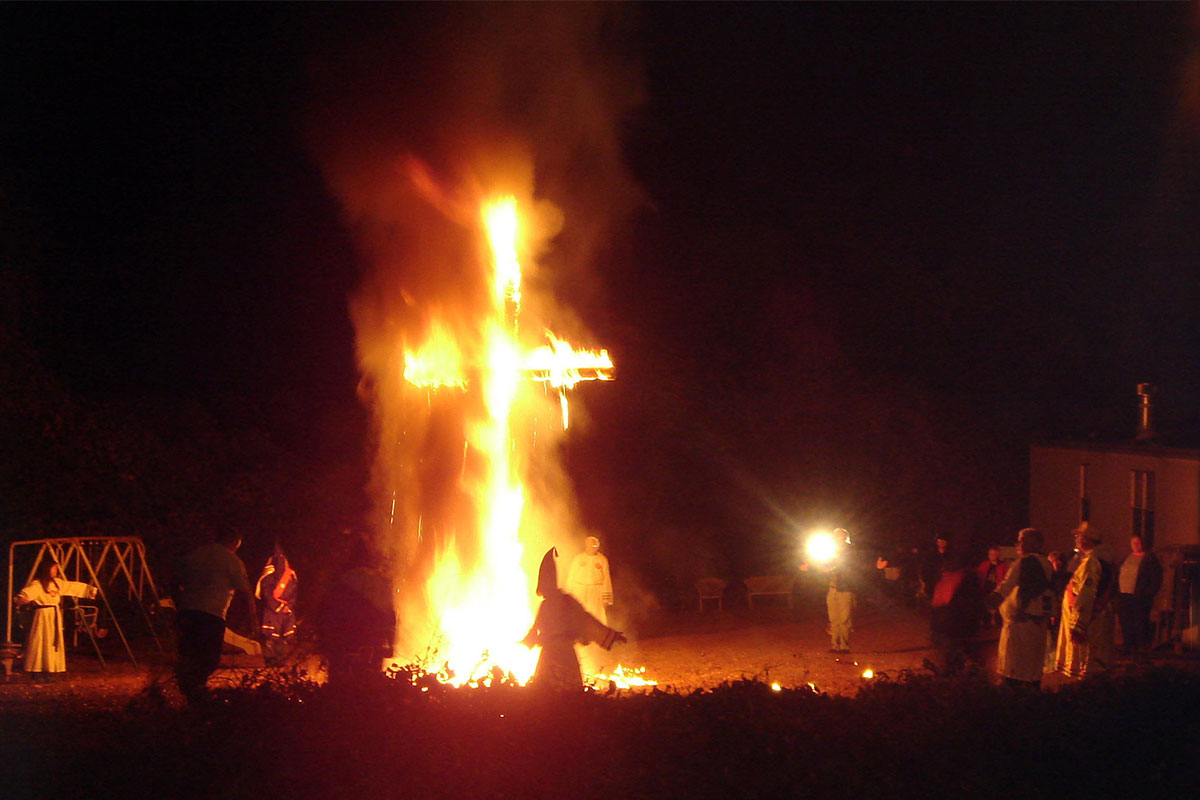 Photo of Ku Klux Klan members standing outside around a giant burning cross