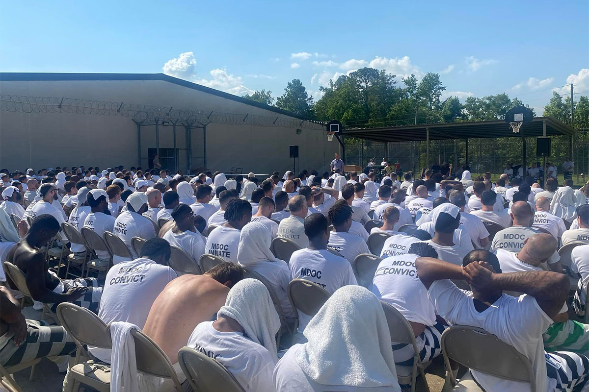 Rows of men in white shirts marked MDOC CONVICT sit in chairs outside of George County Regional Correctional Facility