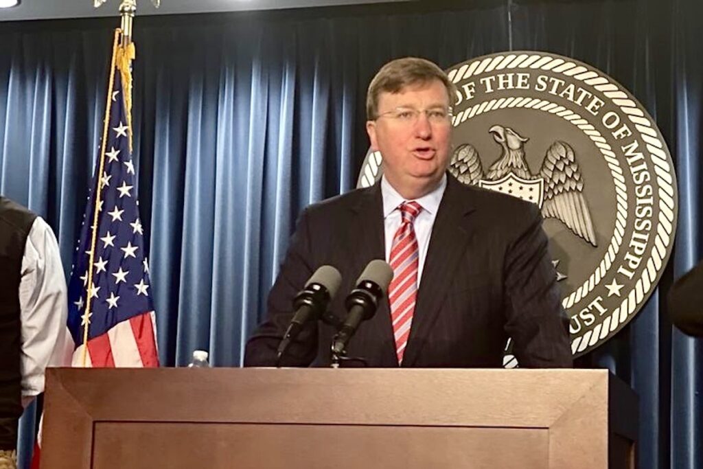 a photo of Tate Reeves at a press conference in front of a state seal and blue curtains