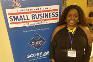 Jillian Smart posing in front of The 2018 American Small Business Championship banner (Mississippi Academic Assessment)