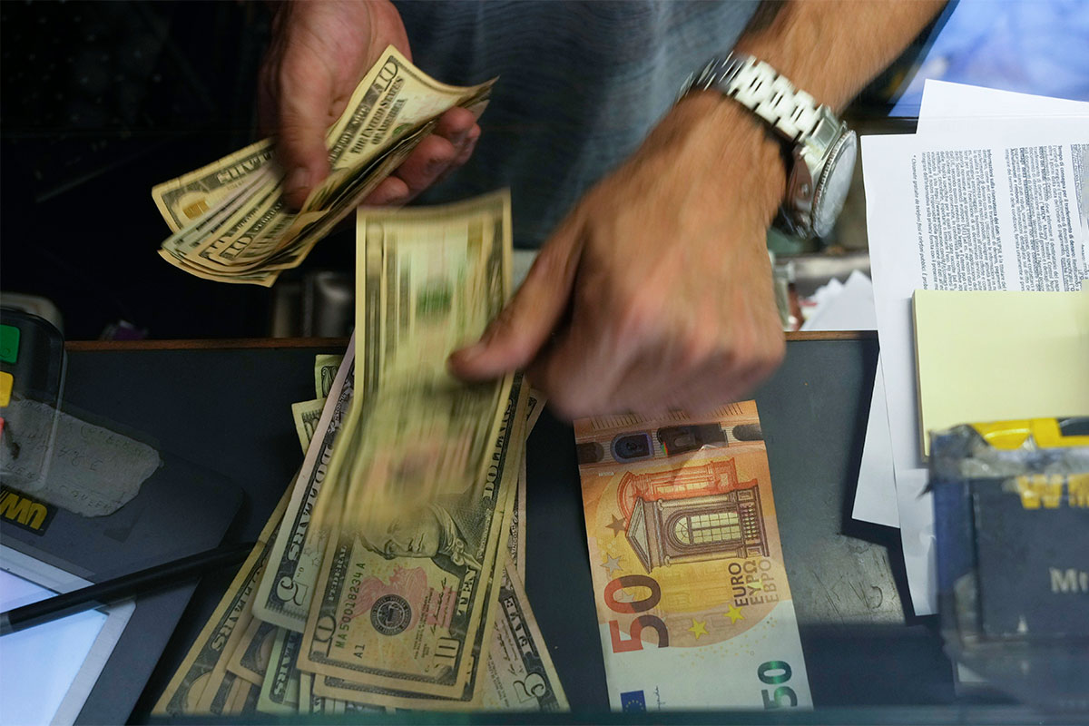 A pair of hands quickly counting a stack of US dollars with 50 euros next to it