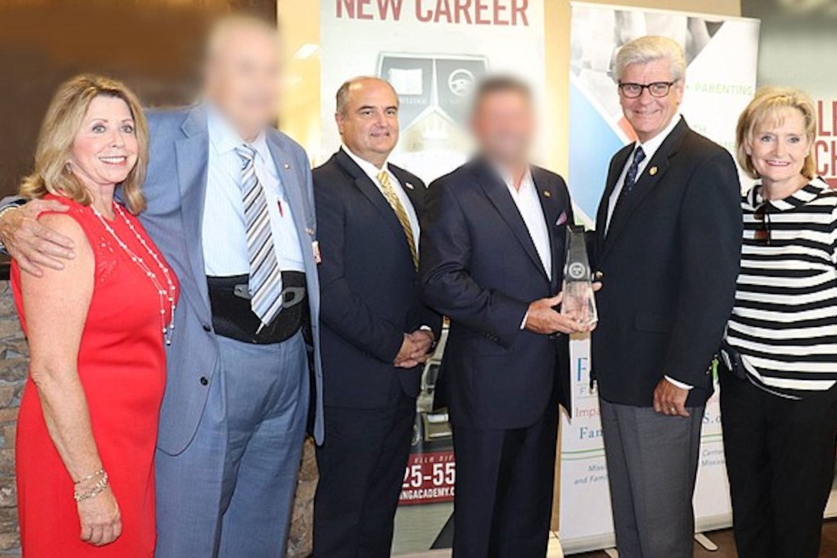 a photo showing Nancy New next to a man whose face is blurred, John Davis in the center, another blurred man's face, Gov. Phil Bryant, and Sen. Cindy Hyde-Smith