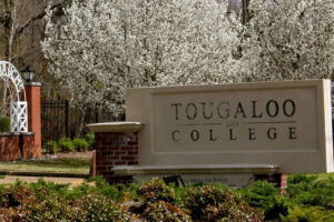 Exterior sign for Tougaloo College with white flowering trees in the background