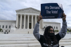 a photo of a man outside the U.S. Supreme Court holding a "We Demand the Vote" sign