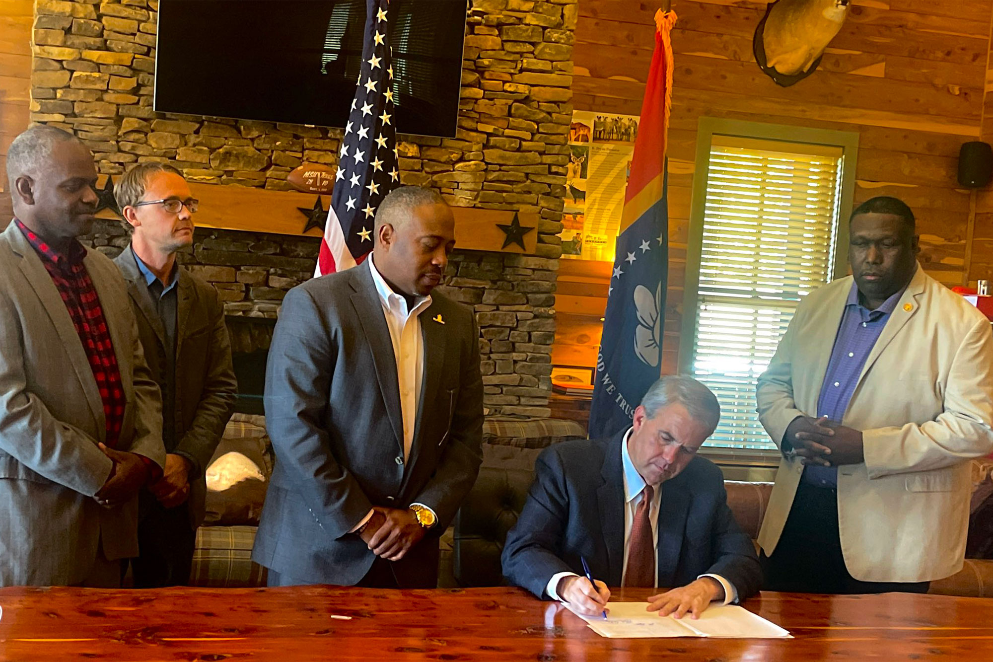 Brandon Presley sits at a table signing a document as four other men look on