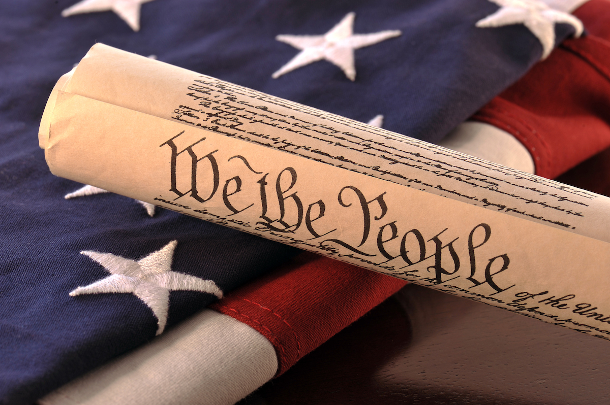 a rolled up constitution displaying "We The People" on top of folded American flag (succession planning)