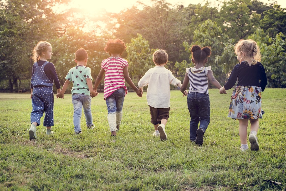 Group of diverse children in a field walking away while holding hands (single mothers)