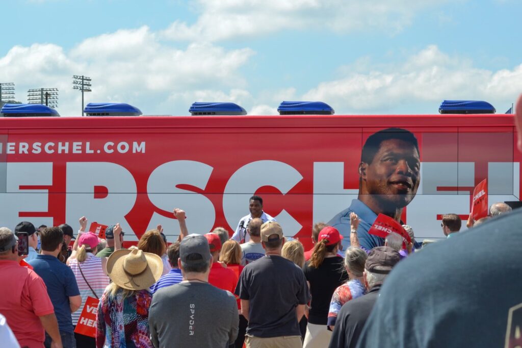 a photo of Herschel Walker standing in front of a crowd, his campaign tour bus behind him