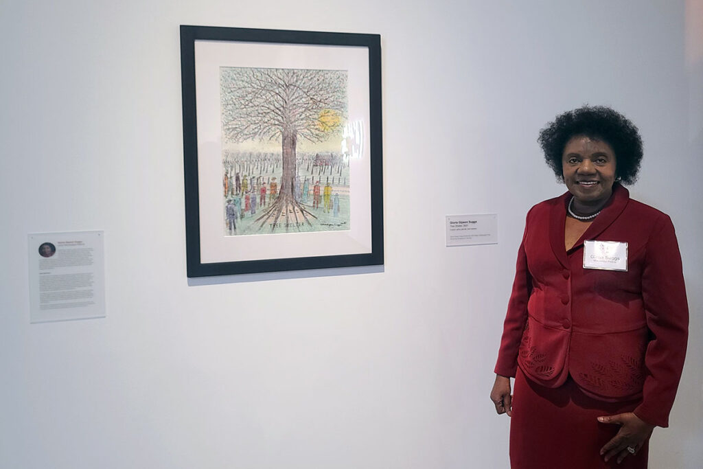 Gloria Gipson Suggs in a red suit dress standing beside a piece of her art Shelter Tree