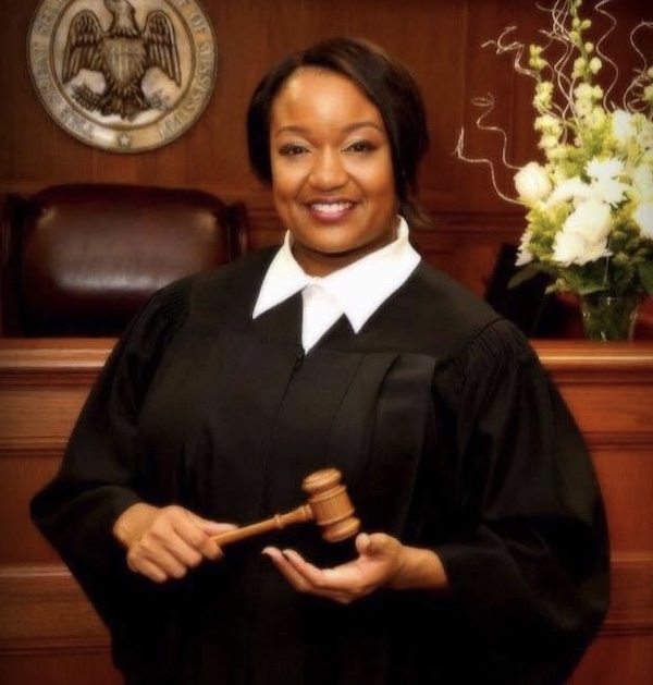a photo of Judge Martin in her courtroom holding a gavel and smiling at the camera