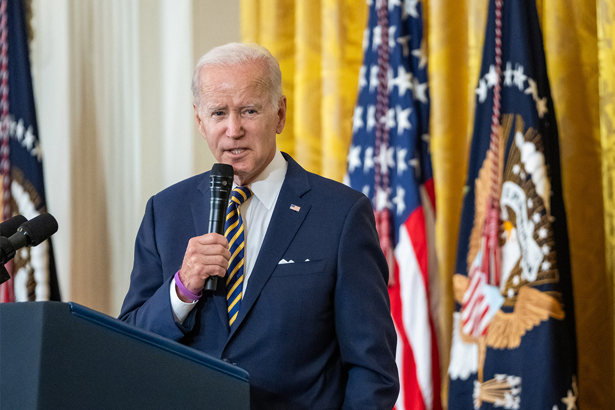 President Joe Biden speaks at a podium, gold curtains and US flag behind him