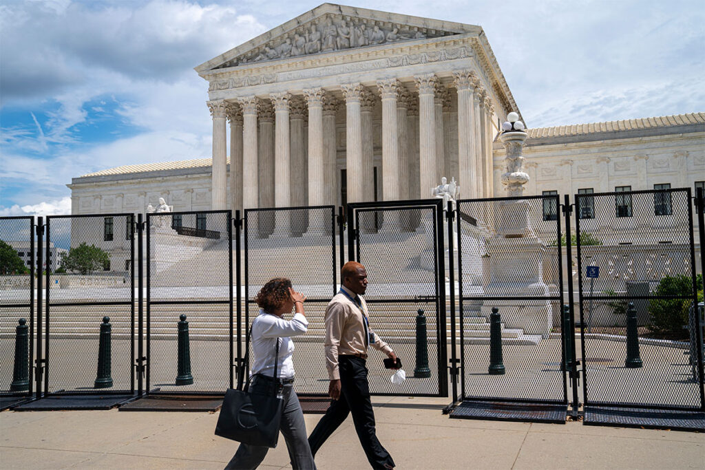 Two people in work attire walk past the temporary black fence barriers that surround the US Supreme Court building