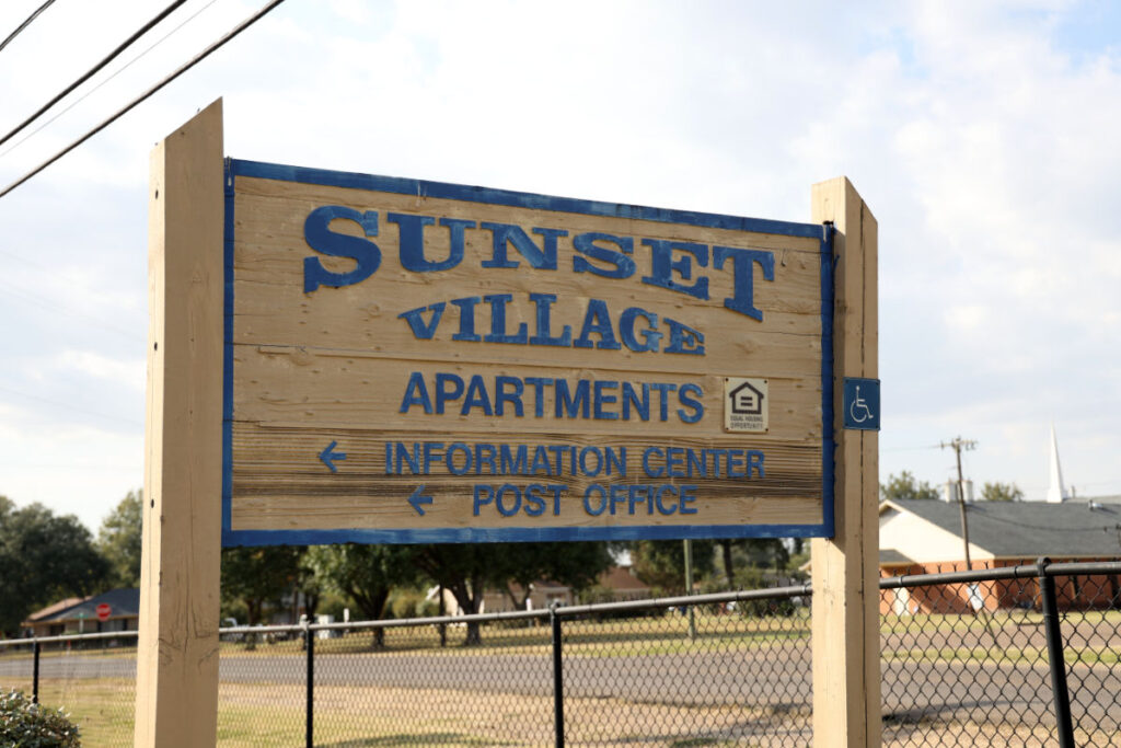 A wooden sign outside that reads Sunset Village Apartments