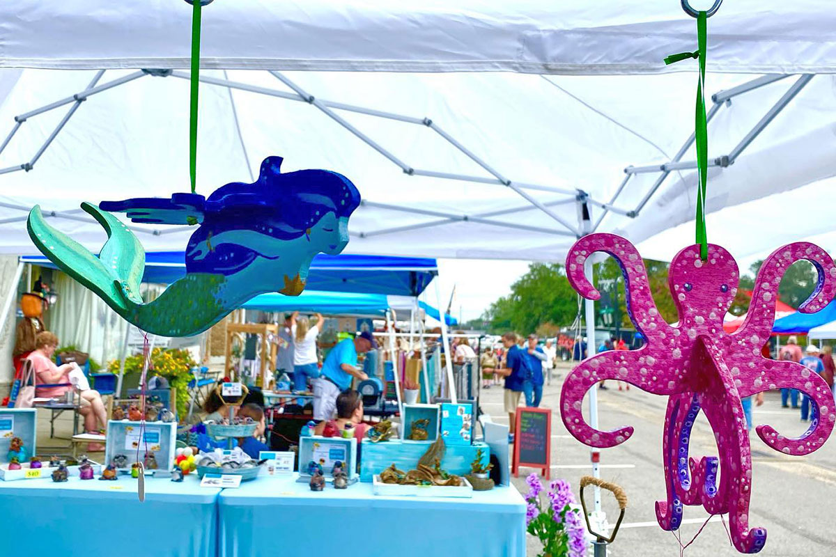 Close-up of a colorful wooden mermaid and octopus ornament hanging on the edge of a vendor tent
