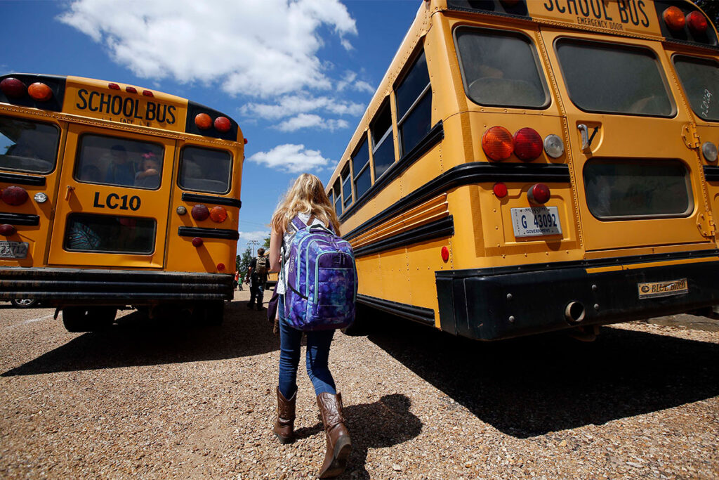 A student carrying a backpack is walking up between two yellow school buses
