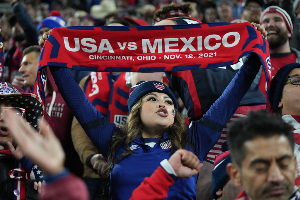 A soccer fan in red and blue holds a USA vs Mexico scarf aloft