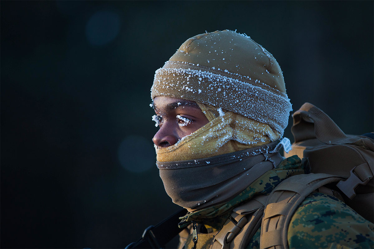 A US Marine in snow gear stands with snow on their face (body warm)