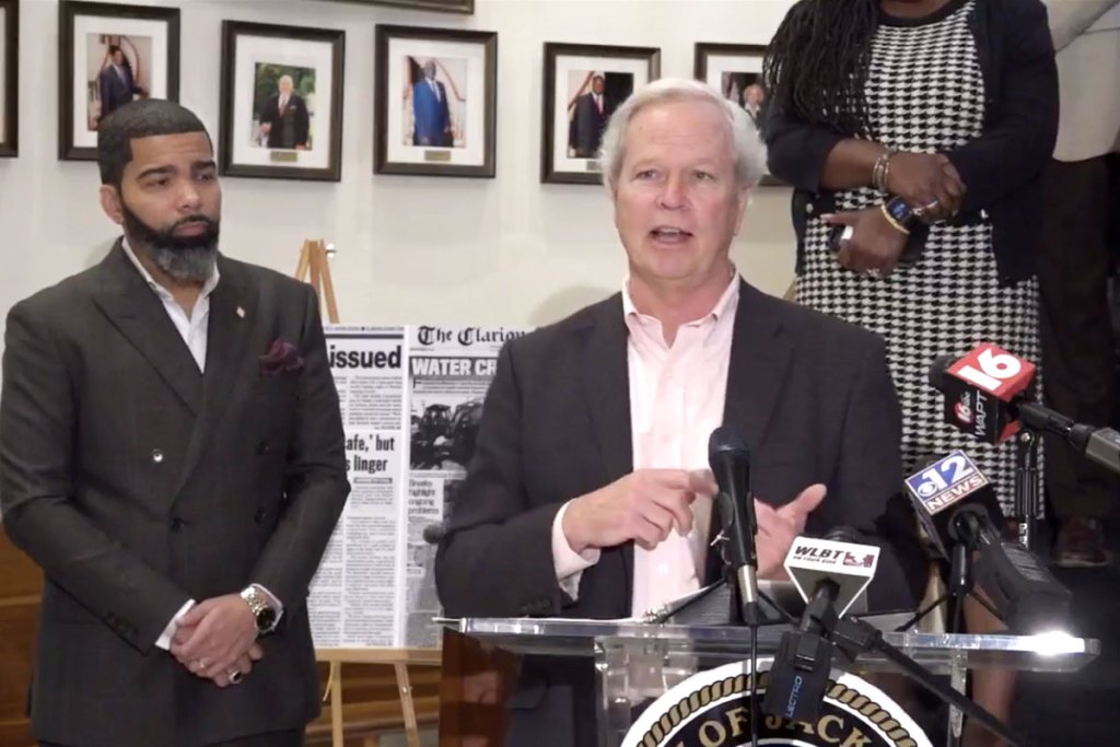 Mayor Chokwe A. Lumumba listens as Ted Henefin speaks at a conference podium