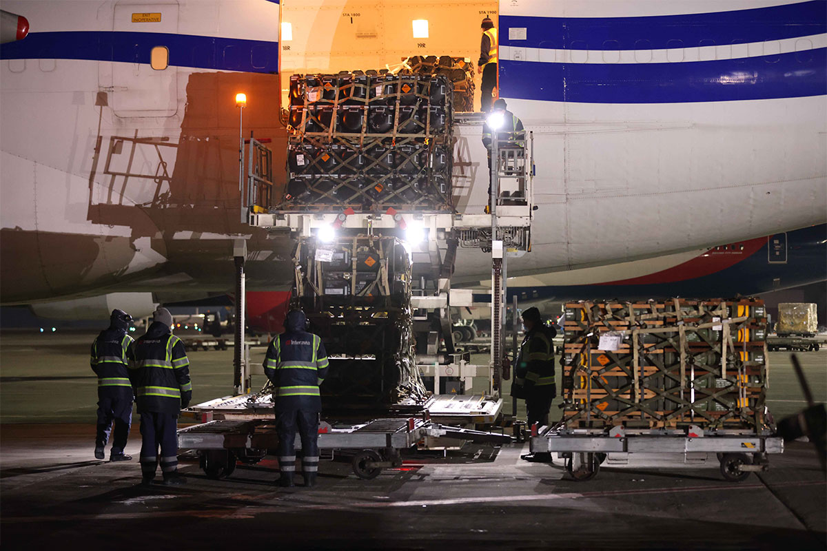 People with reflective vests and dark clothing are seen unloading large boxes from an airplane at nighttime. (Ukraine)