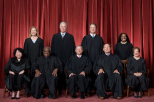 The U.S. Supreme court justices in black robes sitting in two rows in front of red curtains