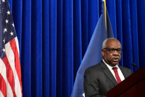 Associate Supreme Court Justice Clarence Thomas speak in front of a blue curtain