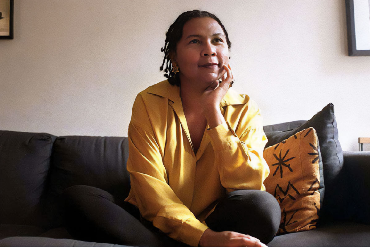 Author bell hooks in a yellow top sitting on a black couch