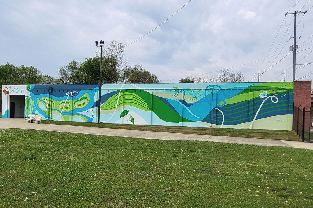 A colorful mural on the side of a brick building done in blues and greens