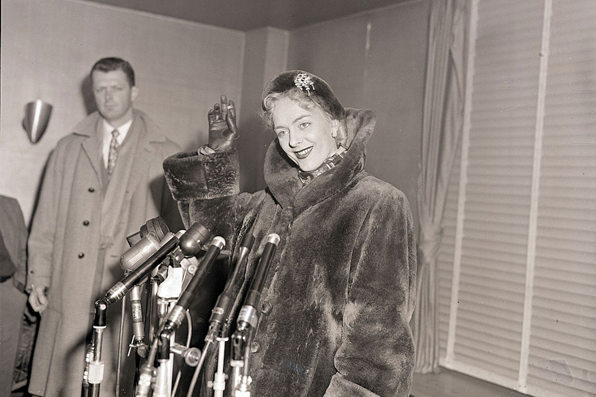 Christine Jorgensen standing before a set of microphones at a press conference (gender-affirming)