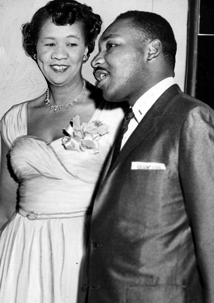 A woman in an evening dress with a corsage stands next to a man in a suit, both smiling and chatting (Black women)