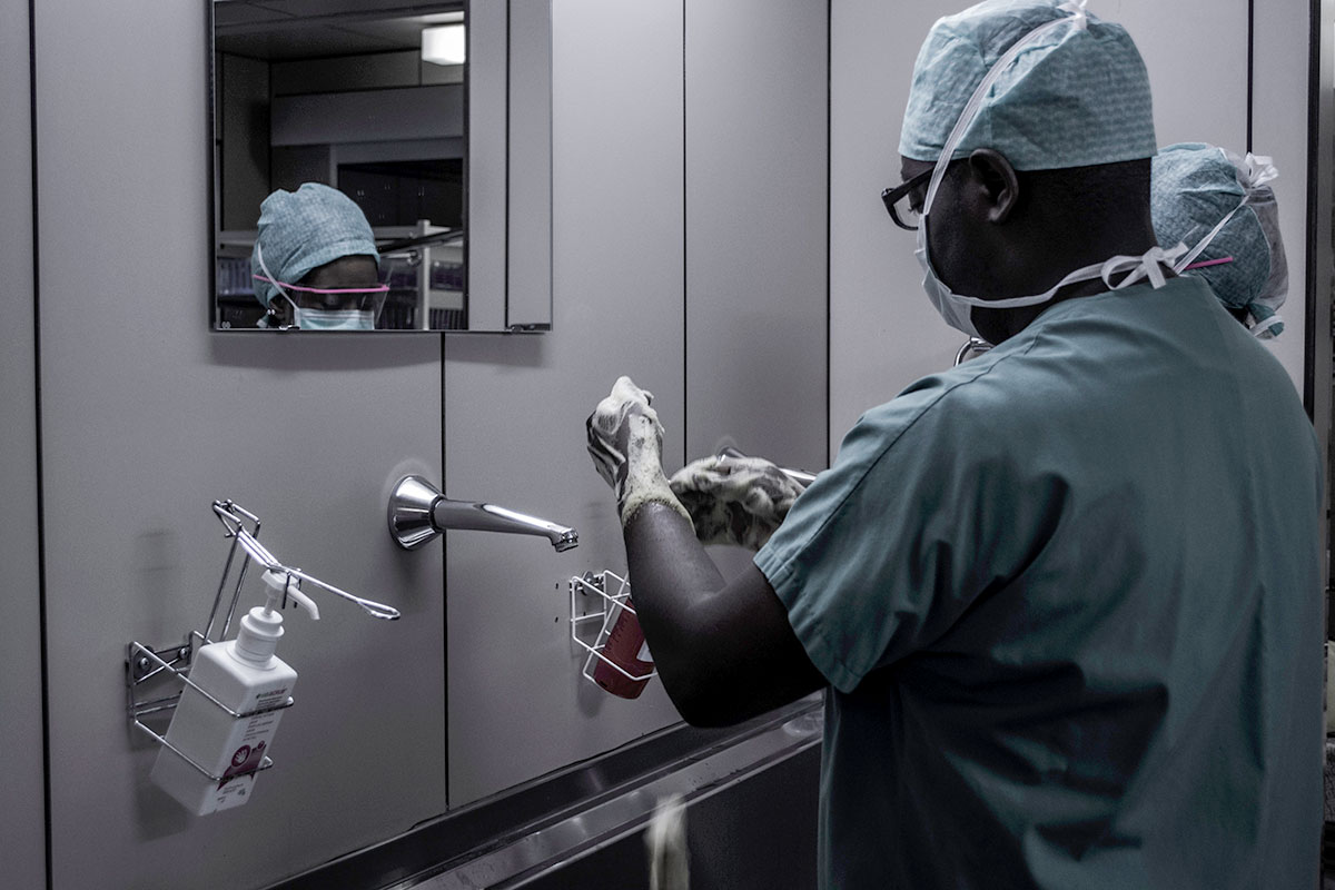 A Black medical professional adjusts gloves in front of a mirror