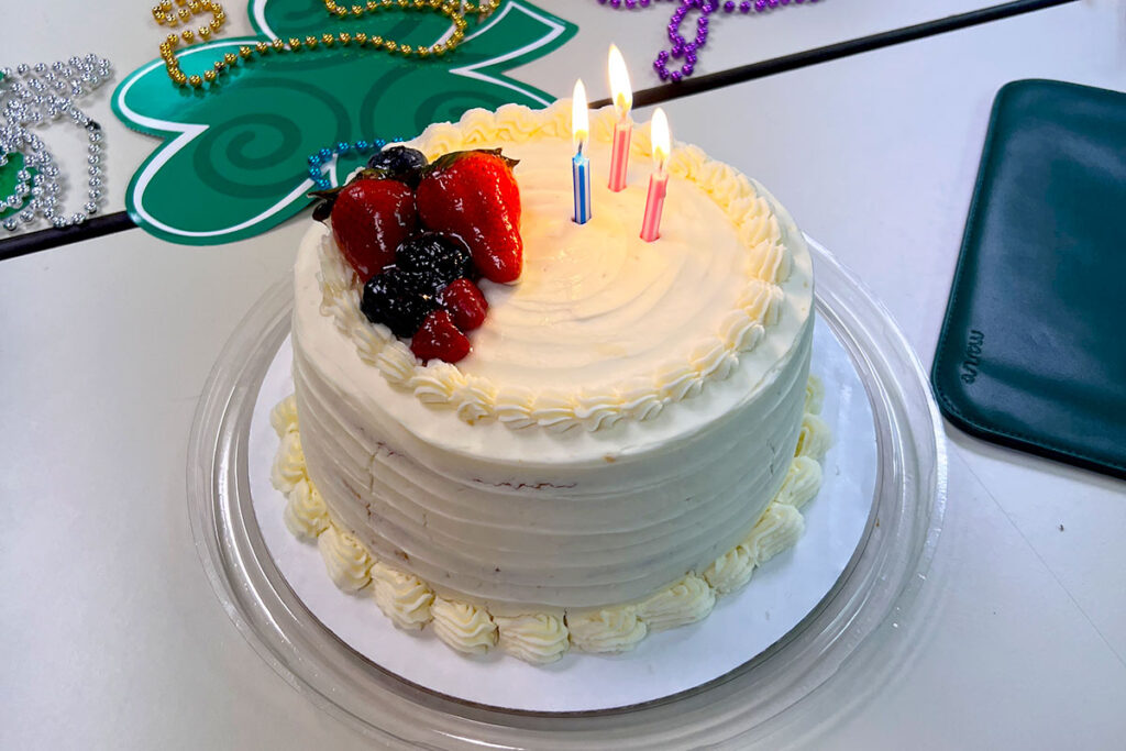 A white birthday cake with fruit on top and 3 lit candles