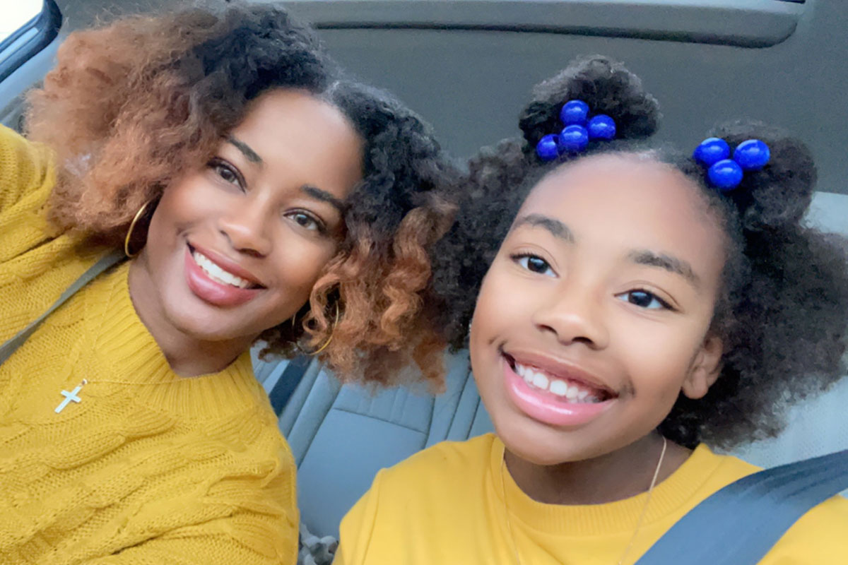 A woman and her daughter smile in a car selfie while both wearing matching mustard yellow colored tops